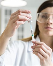 Front view female scientist with safety glasses holding syringe with vaccine
