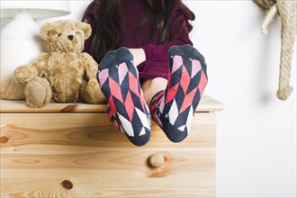 Girl sitting near soft toy showing her feet with multi colored socks