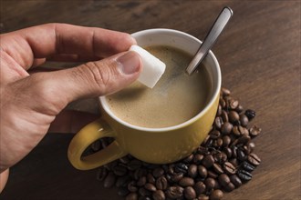 Hand holding sugar near cup with coffee