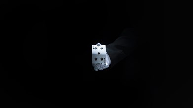 Magician s hand showing club playing card against black background