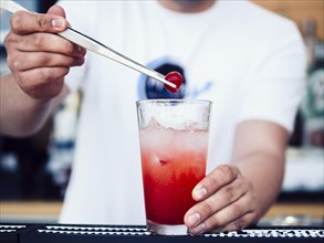 Male bartender decorating drink with cherry