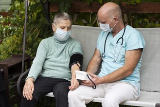 Male nurse using blood pressure monitor older woman