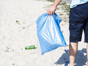 Man s hand carrying blue garbage bag beach
