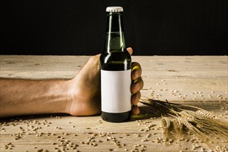 Man s hand holding beer bottle with ears wheat wooden surface
