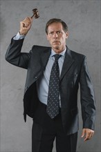 Mature male lawyer hitting with gavel against gray textured background