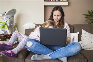 Mother with her daughter sitting sofa using laptop
