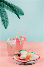 Palm leaves grapefruit cocktail glasses popsicles coral desk against teal background