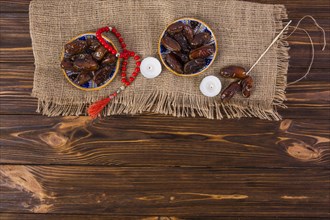 Plate juicy dates with red prayer beads lighted candle wooden desk