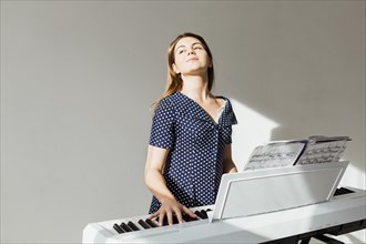Portrait young woman playing piano standing against white wall