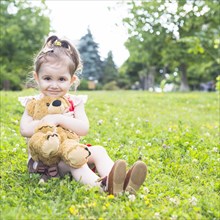 Pretty girl sitting green grass cuddling her teddy bear