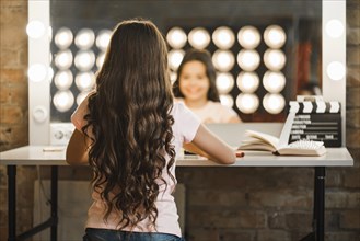 Rear view girl with long brunette wavy hair sitting makeup room