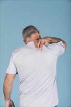 Rear view man suffering from neck pain front blue backdrop
