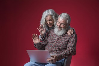 Senior couple looking laptop waving their hands against red background