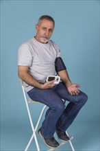 Senior man sitting chair checking blood pressure electric tonometer