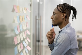 Side view man thinking office while looking sticky notes