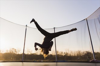 Silhouette girl jumping trampoline doing split