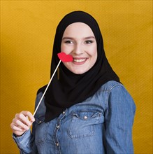 Smiling muslim woman holding paper prop shape red lips backdrop
