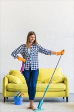 Smiling young woman standing with mop pink napkin living room