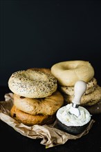 Stacked different type bagel with cheese bowl against black backdrop