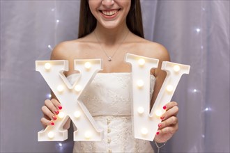 Teenage girl celebrating quinceanera while holding roman numerals
