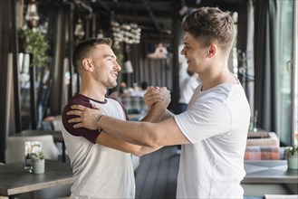 Two happy young male friends shaking hands restaurant