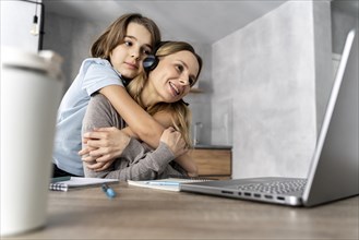 Woman with headset working laptop hugged by girl