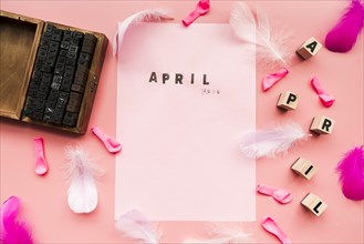 Wooden typographic blocks balloons feather april blocks april stamp white paper against pink backdrop