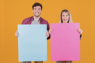 Young businesswoman businessman holding blue pink placard against orange background