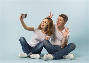 Young couple taking selfie mobile phone against blue background