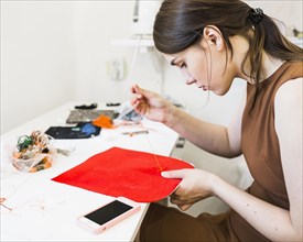 Young woman sewing red cloth with needle