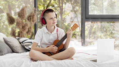 Boy with headphones playing ukulele long shot