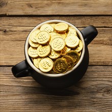 Cauldron with gold coins wooden background