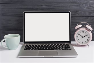 Ceramics cup alarm clock open laptop white desk against wooden black background