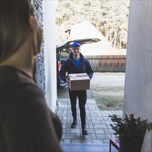 Cheerful delivery man carrying box customer