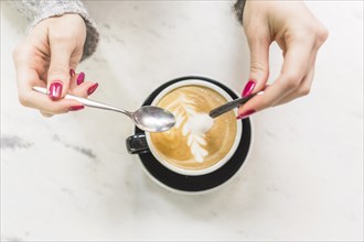 Crop hands pouring sugar into cappuccino cup