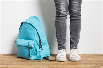 Faceless person standing beside schoolbag wooden table