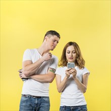 Jealous boyfriend spying his girlfriend watching her phone against yellow background