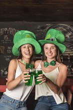 Laughing young women saint patricks hats hugging holding glasses drink bar counter