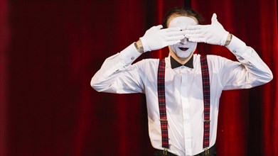 Male mime artist standing front curtain covering his eyes with hands