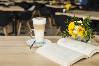 Open book with latte coffee cup fresh flower vase wooden table