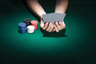 Person hand holding playing card with stacking poker chips casino table