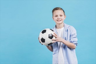 Portrait smiling boy holding soccer ball hand standing against blue sky