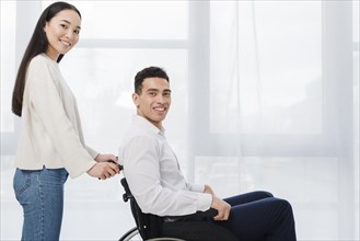 Portrait smiling young woman standing man sitting wheel chair looking camera