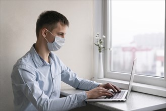 Side view man with medical mask working smartphone