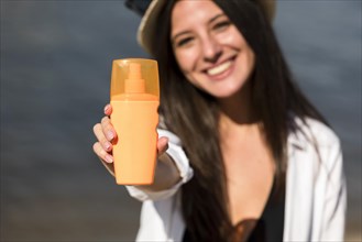 Smiley woman holding bottle sunscreen beach