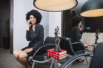 Smiling african american woman talking smartphone armchair office