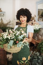 Smiling female florist holding basket flowers
