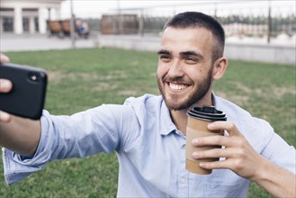 Smiling man taking selfie while holding disposable coffee cup park