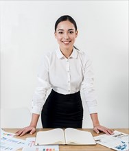 Smiling portrait young businesswoman standing desk against white wall