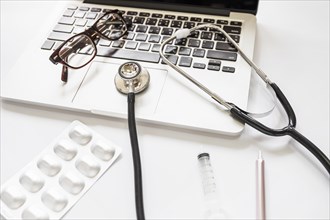 Stethoscope eyeglasses laptop keypad with medicine pack syringe pen white background